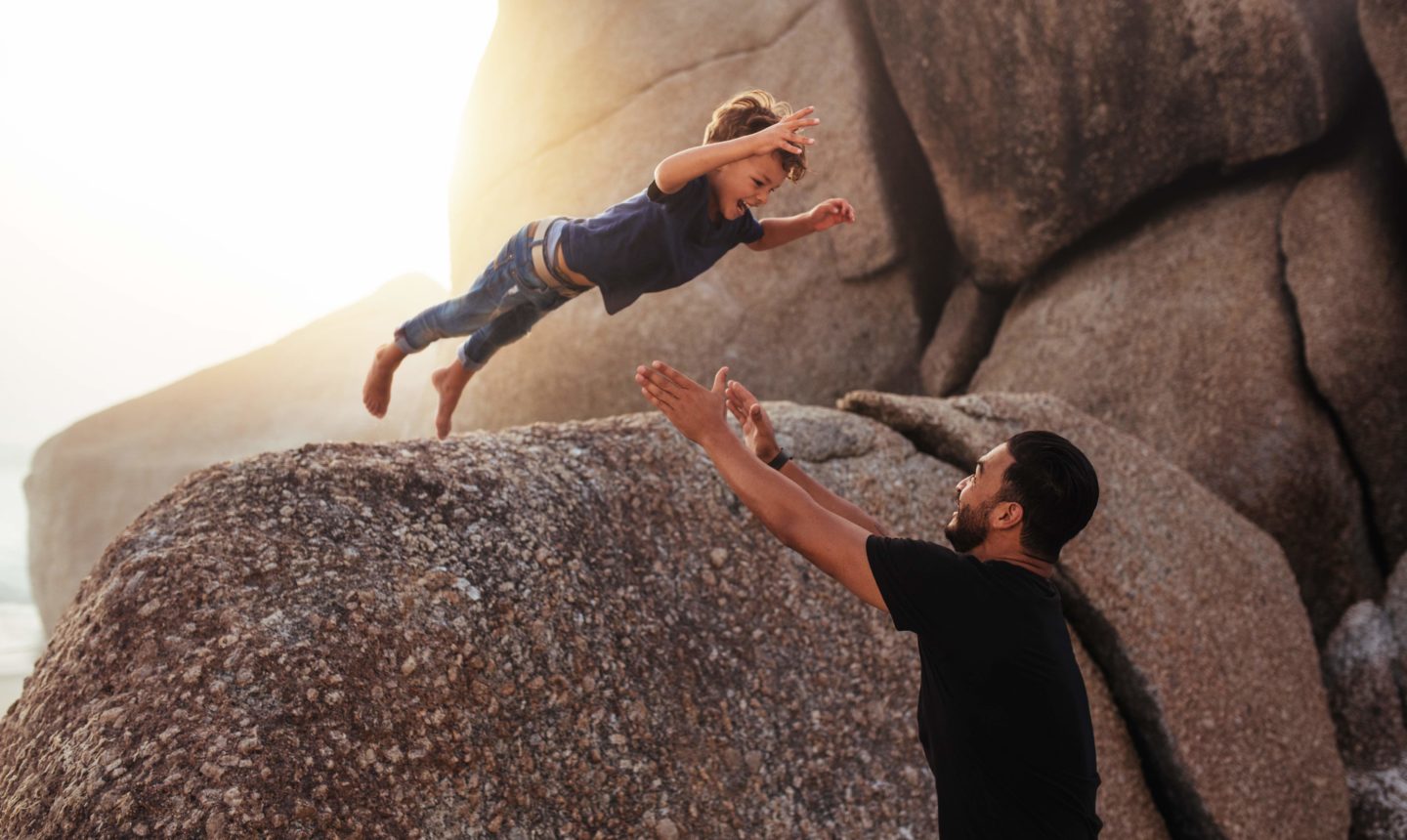 little boy leaping into an adults arms from a big rock