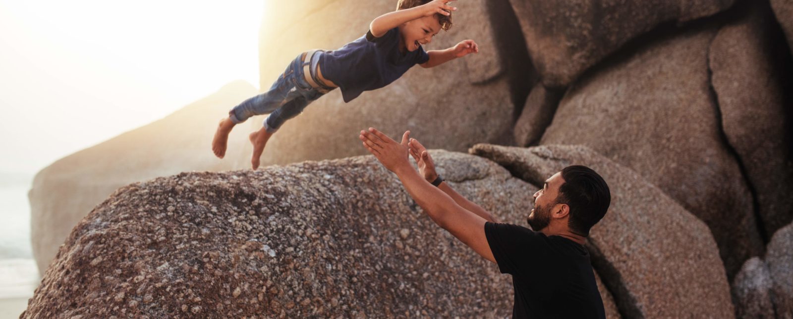 little boy leaping into an adults arms from a big rock