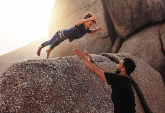 little boy leaping into an adults arms from a big rock