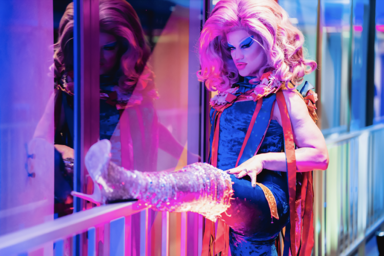 Drag queen wearing knee length boots, with leg up on a guard rail.