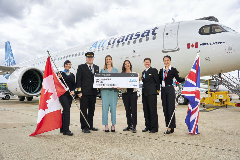 Flight crew members in uniform, one on the right is holding a British flag and the one on the left is holding a Canadian flag. In the background is a 