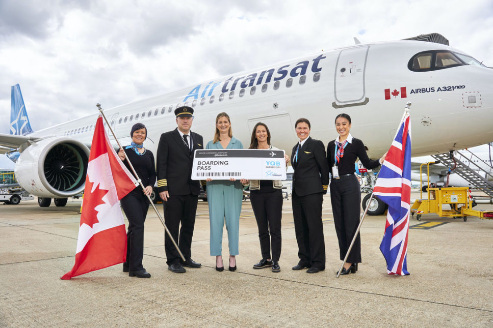 Flight crew members in uniform, one on the right is holding a British flag and the one on the left is holding a Canadian flag. In the background is a
