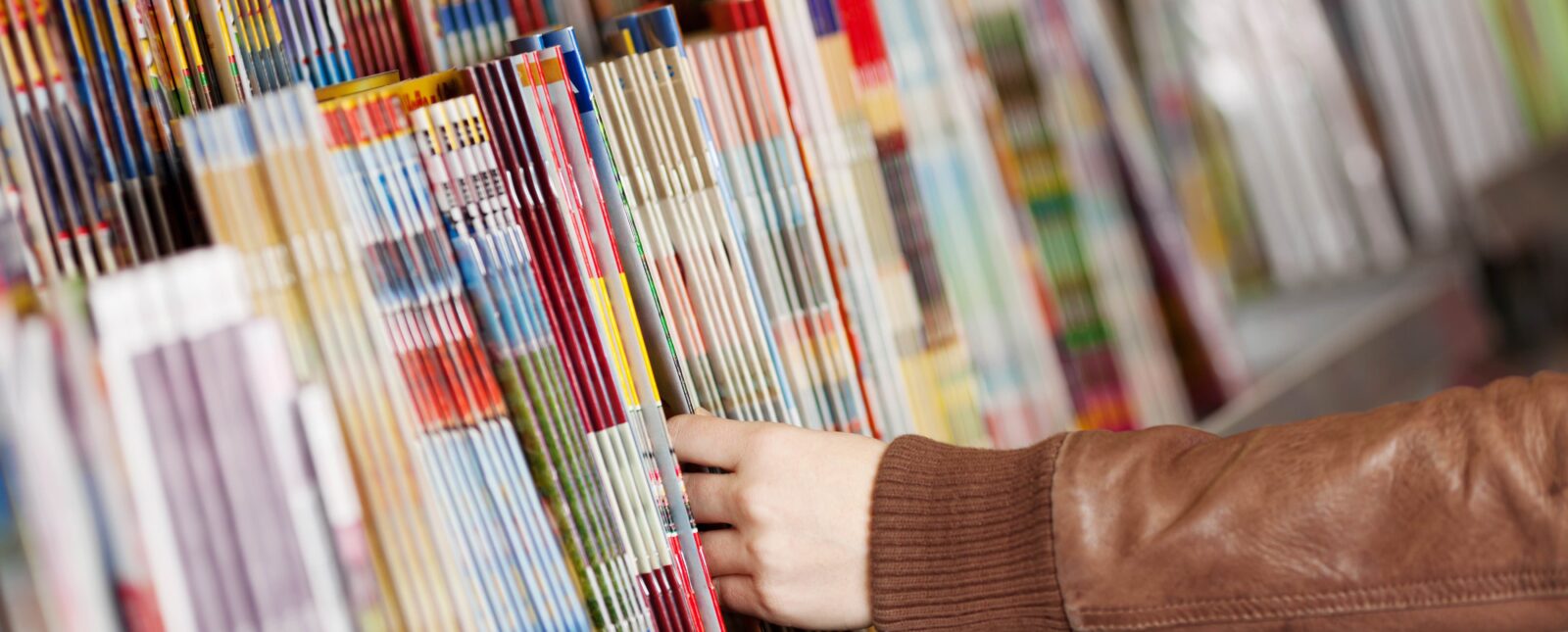 Closeup of woman's hands choosing magazines from shelf in supermarket