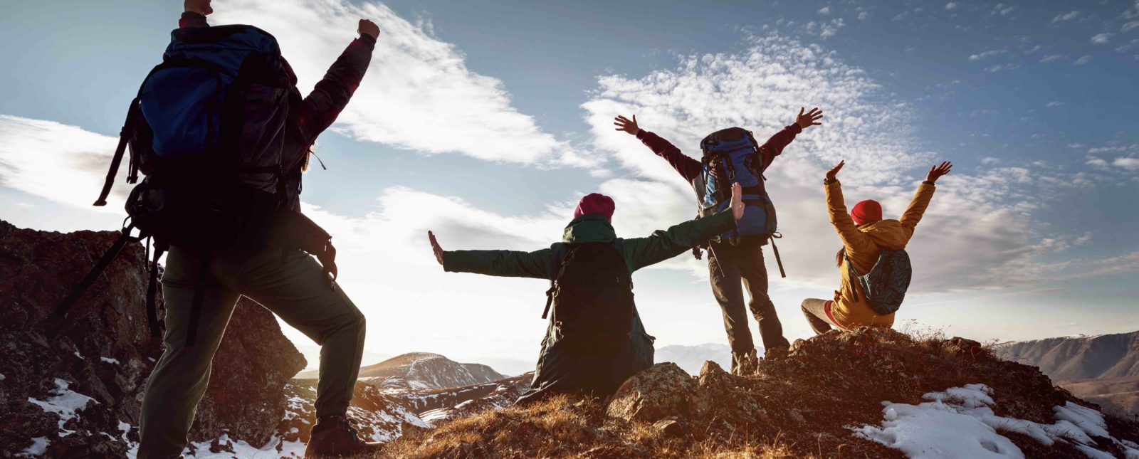 Four happy hikers stands in winner poses at mountain top at sunset time