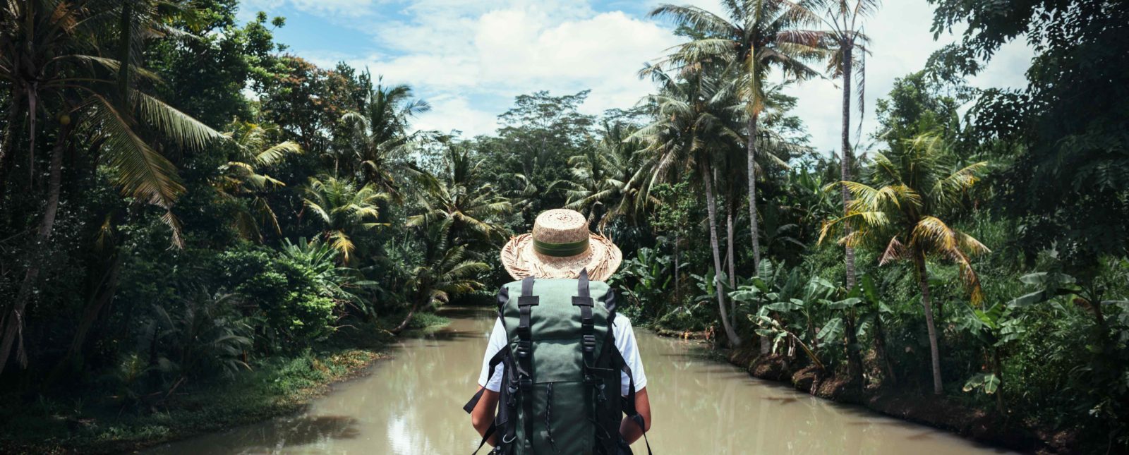 woman with backpack and straw hat looking at tropical river at sunny day