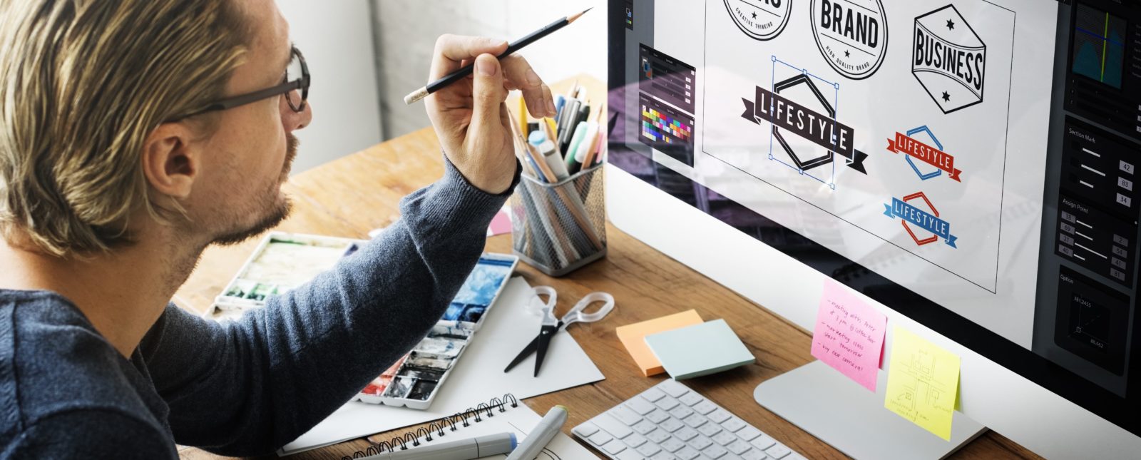 Man with glasses (side profile ) at his desk designing logos on his computer