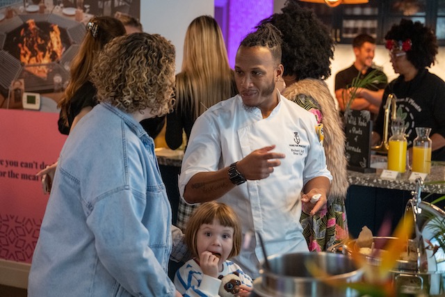 Bermudan chef chatting with a women and a child is below her