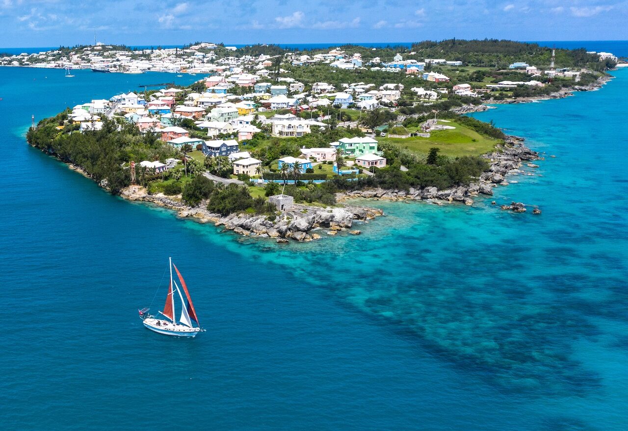 Small colorful island, clear waters, and a sailboat.