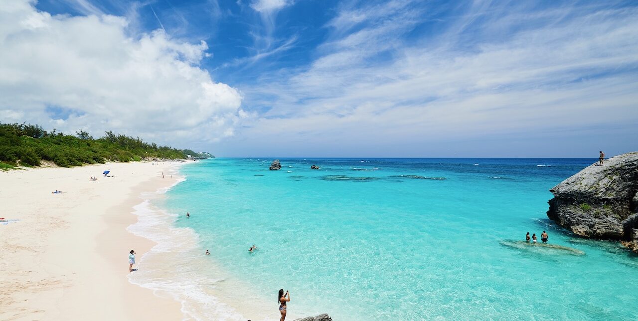 Blue waters and sandy beach. People standing on rocks