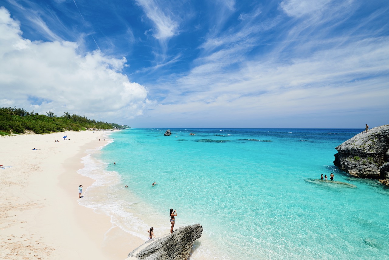 Blue waters and sandy beach. People standing on rocks