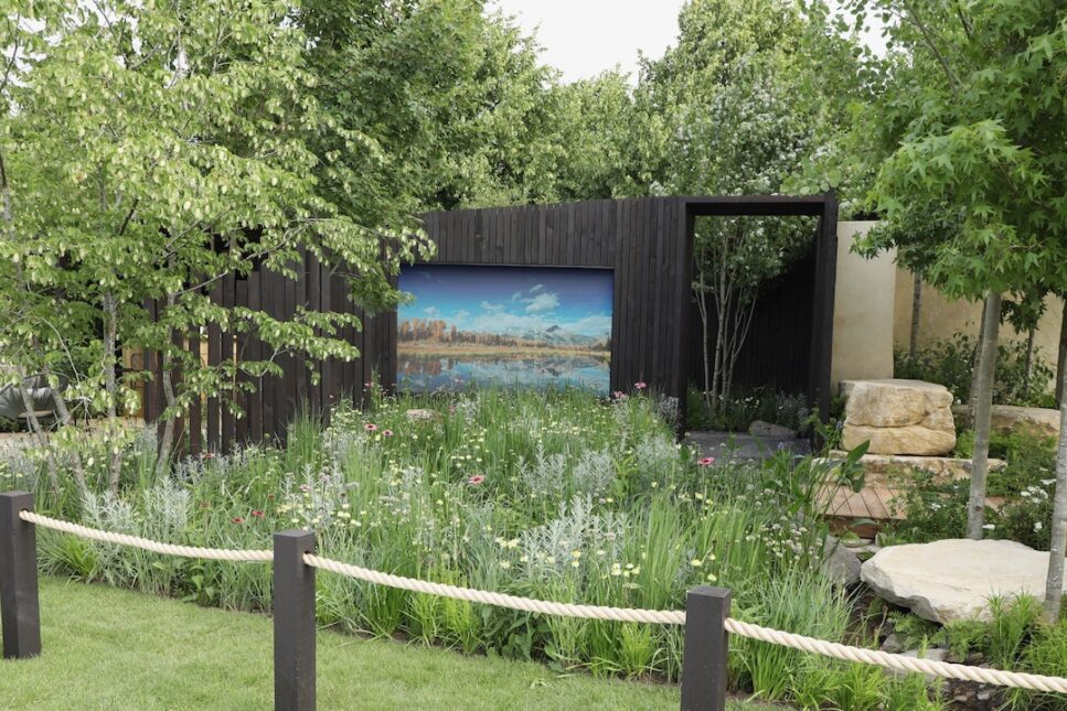 A garden with a wooden wall and a trail behind the wall. The garden is blocked off with ropes