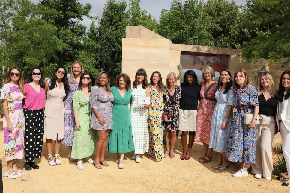 A diverse group of 16 women standing together smiling in a garden